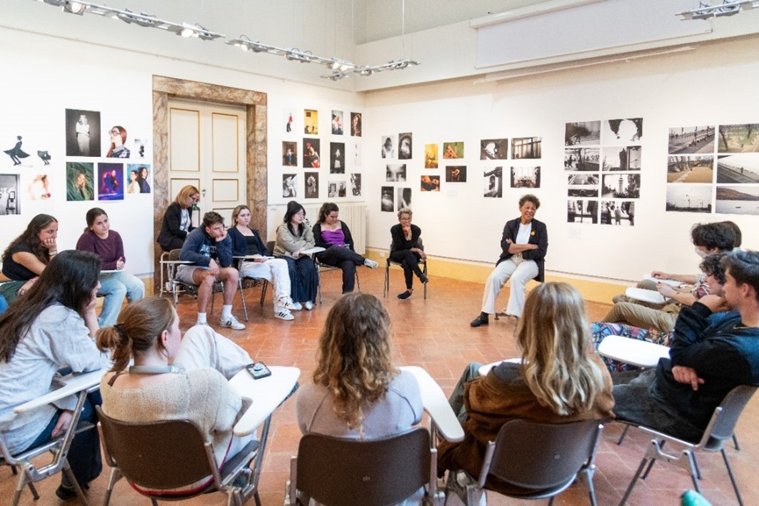 A group of people sit in chairs in a circle. On the walls behind them is artwork.