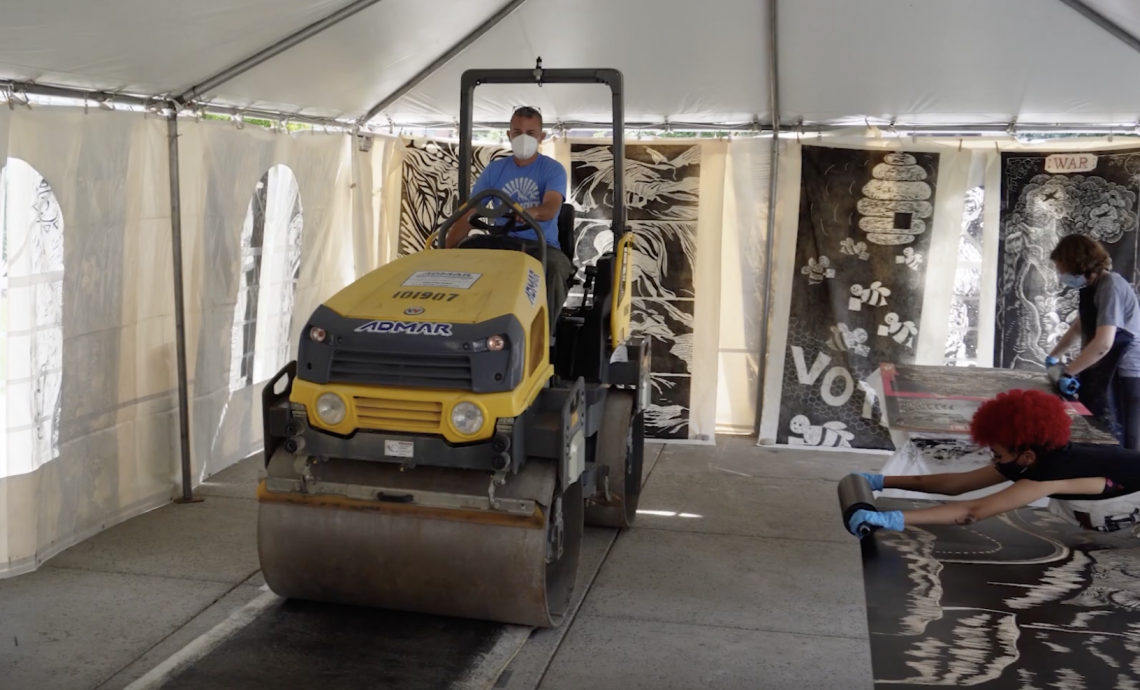 A person drives a steamroller over a printed artwork