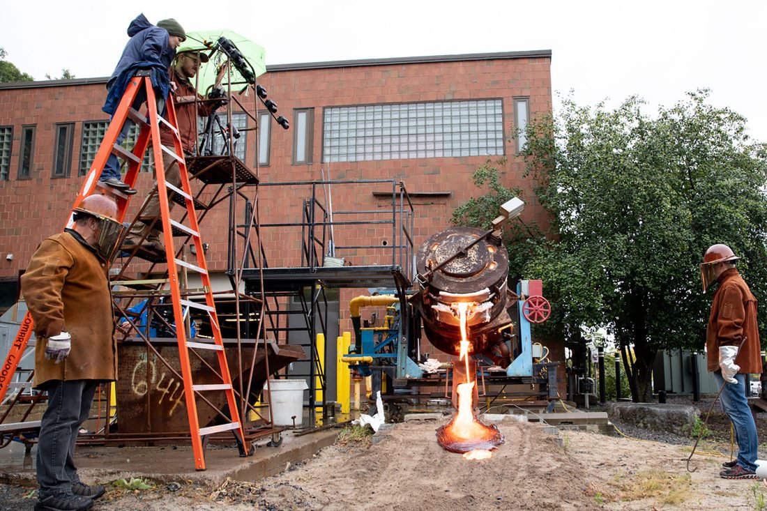 A group of people pour lava from a large cauldron