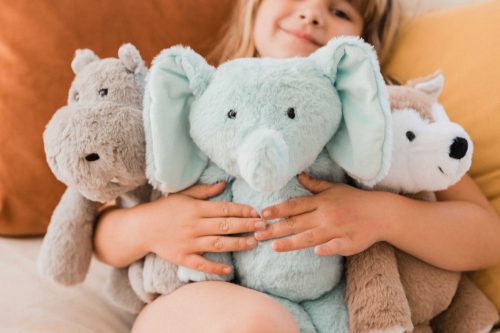 A child holds a stuffed hippo, a stuffed elephant, and a stuffed fox
